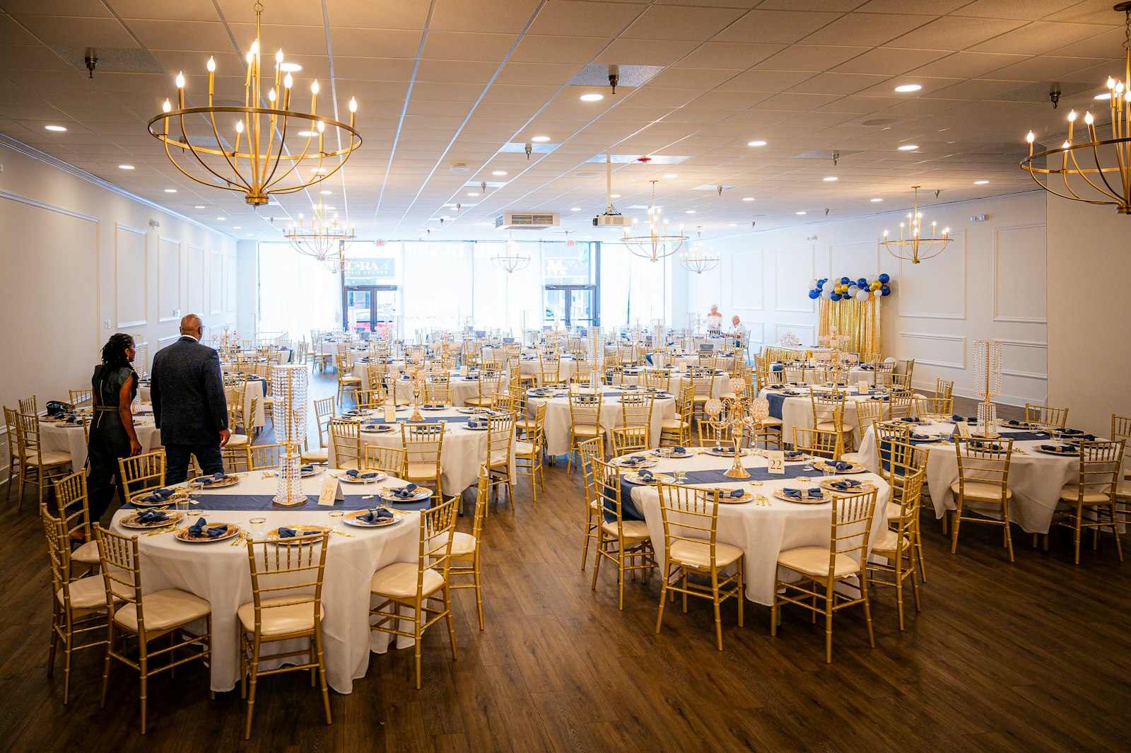 An empty banquet hall set with round tables, place settings, and chandeliers, waiting for guests.