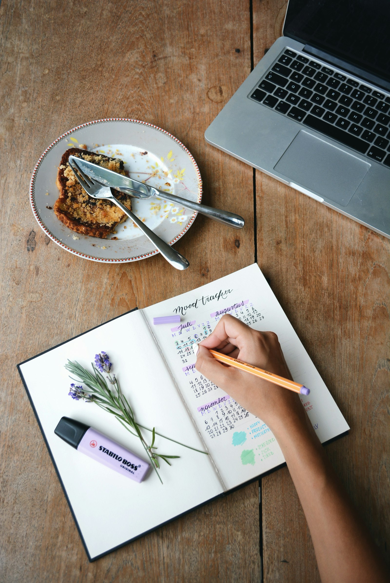 A hand holding a pen over an open journal, with a highlighter beside it.