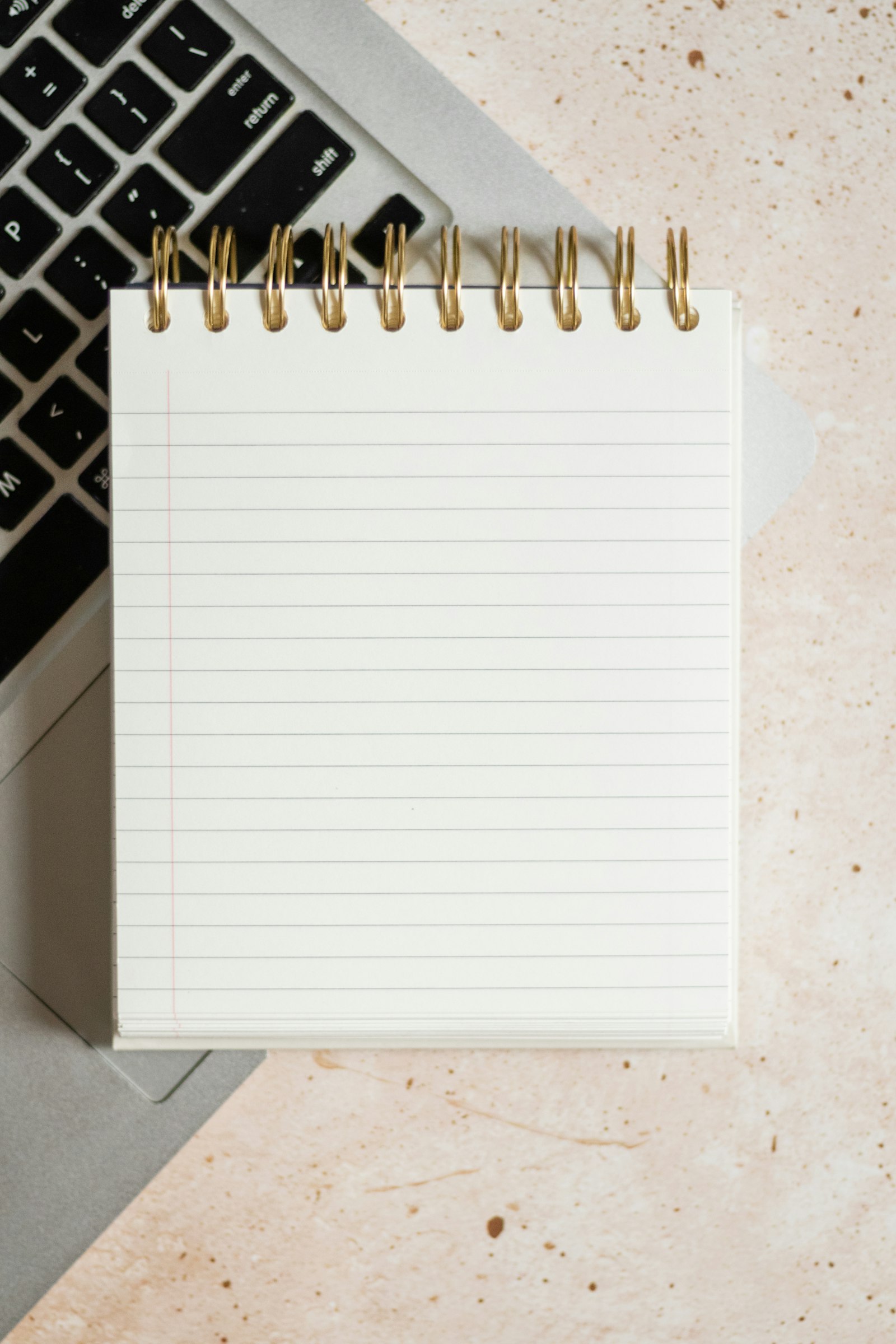 A notepad and pen resting on a laptop beside a keyboard, glasses, and a calendar.