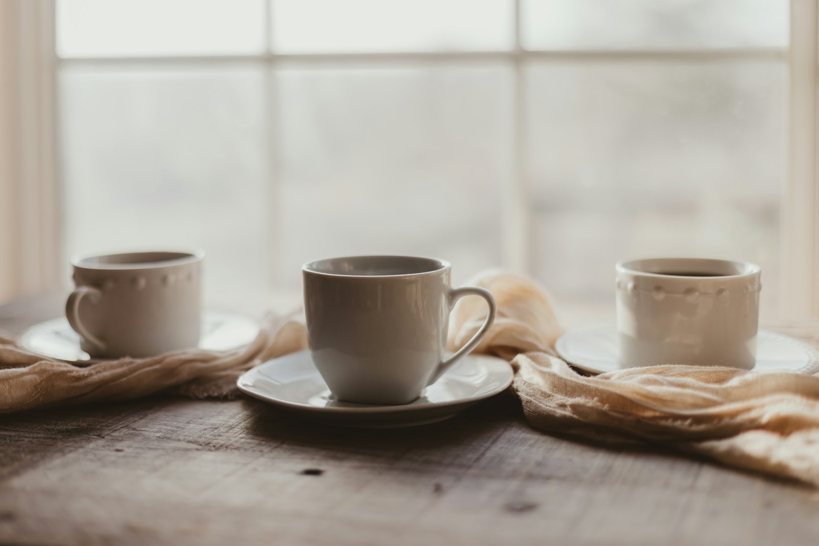 Two cups of coffee on a wooden table in window light.