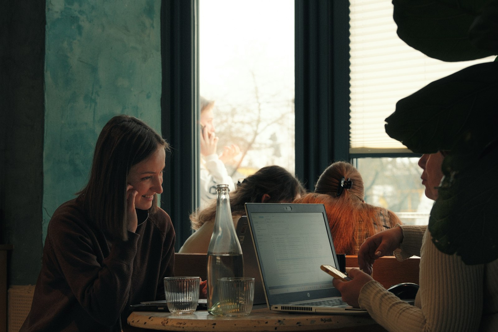 Two women in conversation at a café table, a laptop open between them.