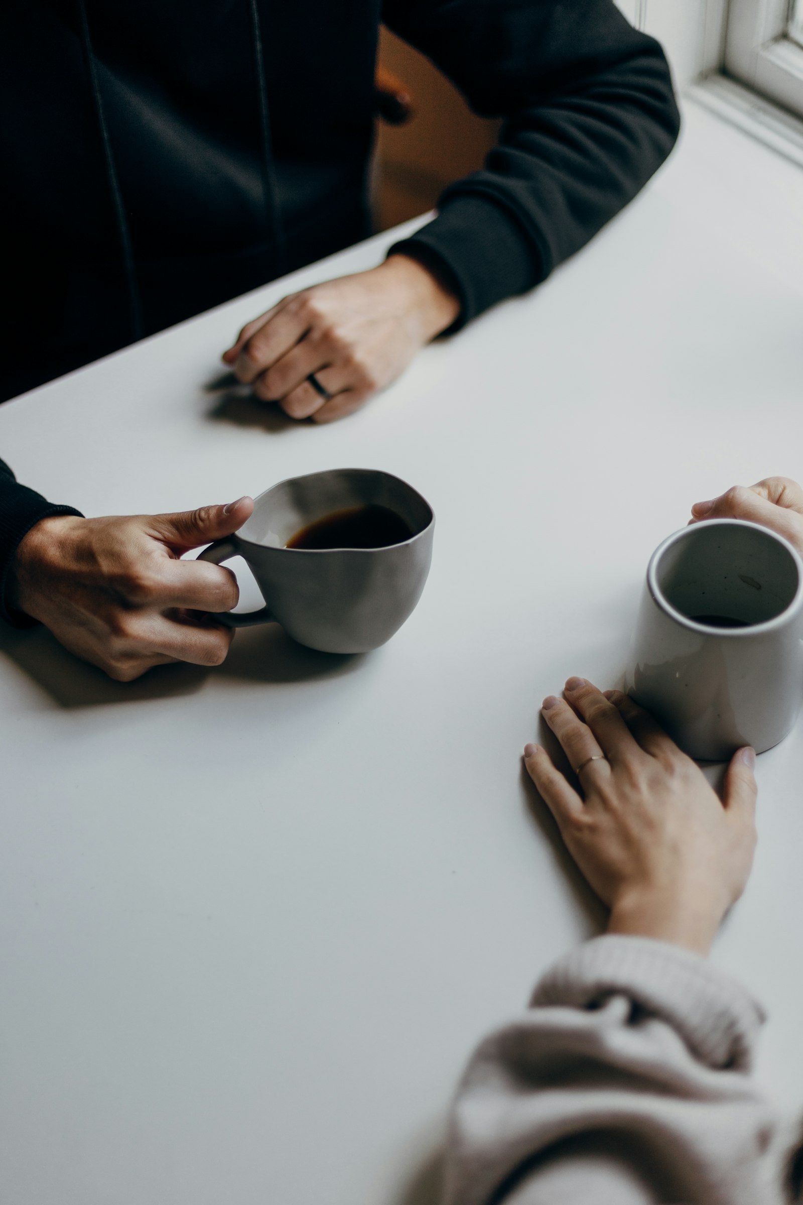 Two people talking across a café table over cups of coffee.