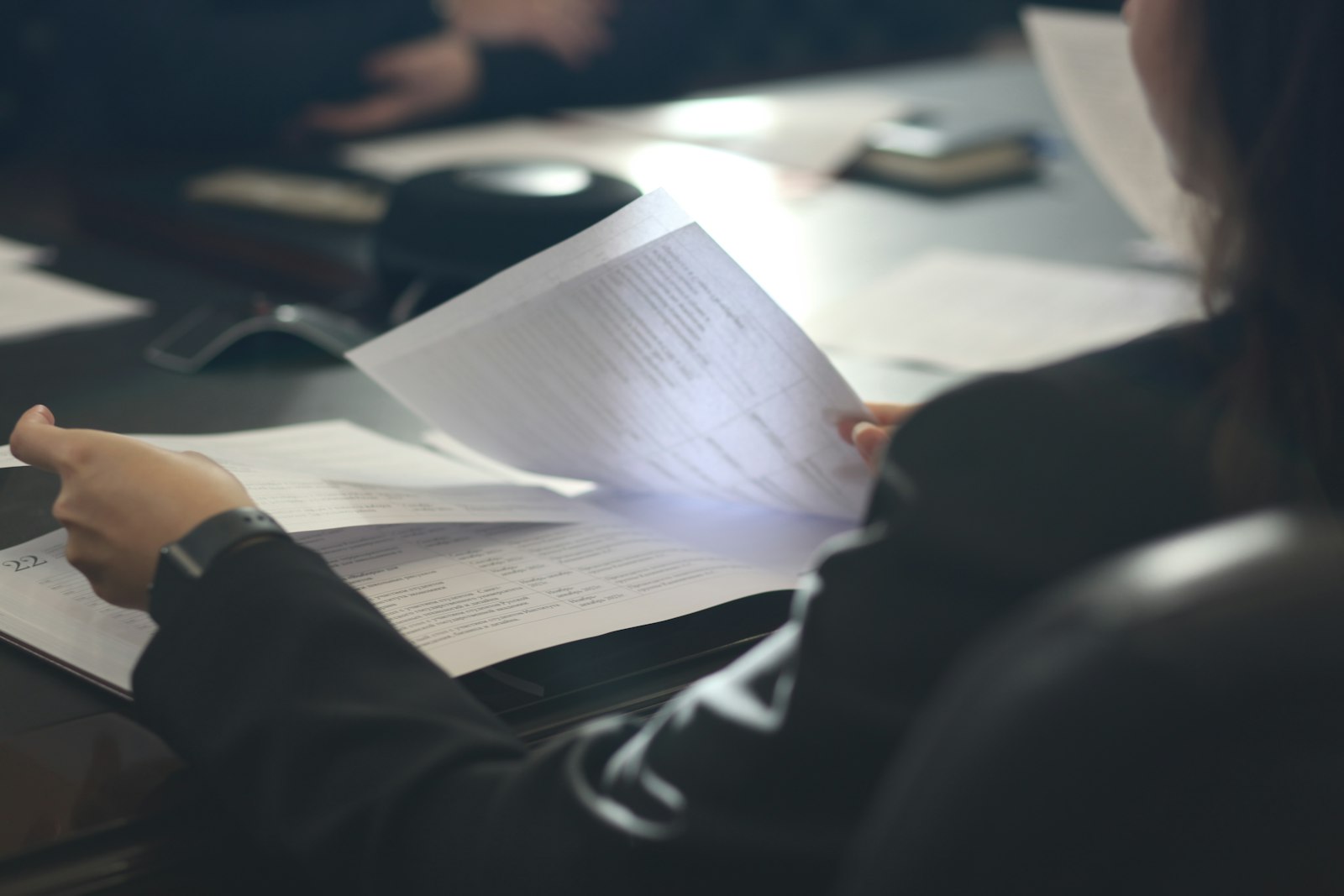 A woman seated at a table, reading a printed document.